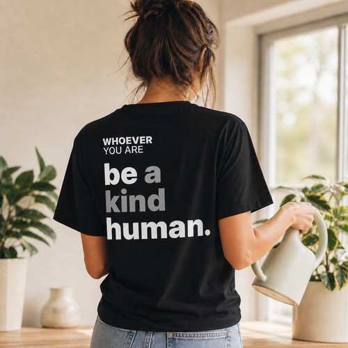 Person wearing a black Be a Kind Human kindness t-shirt with meaningful back print at home