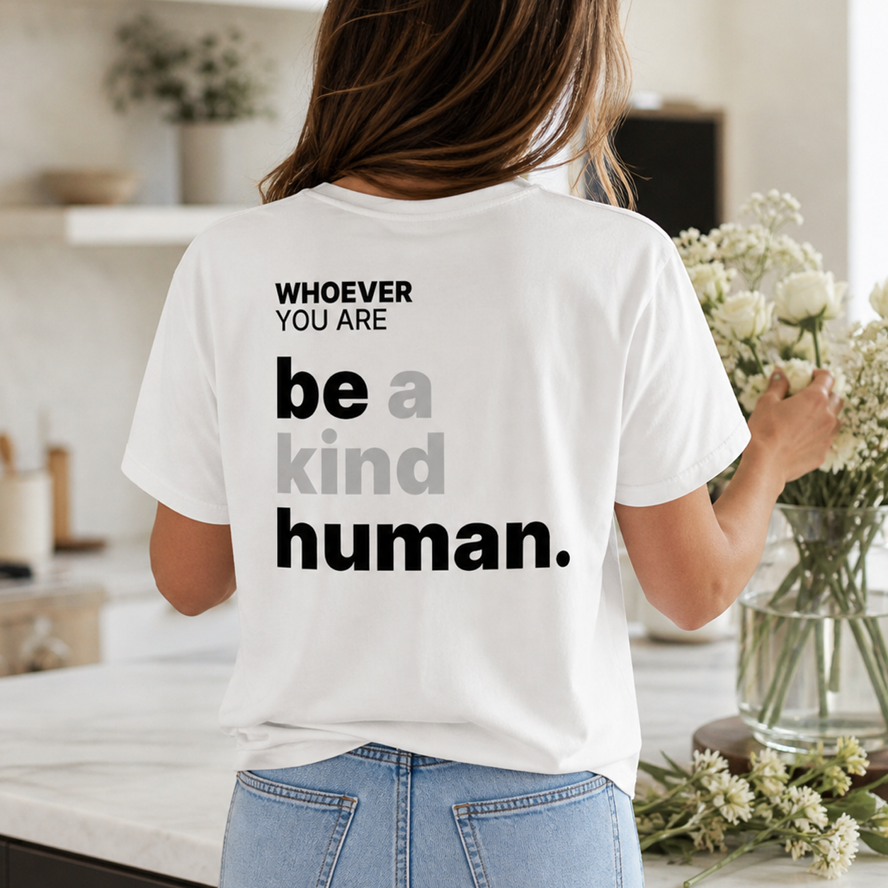 Person wearing a white Be a Kind Human t-shirt in an everyday setting with back print visible