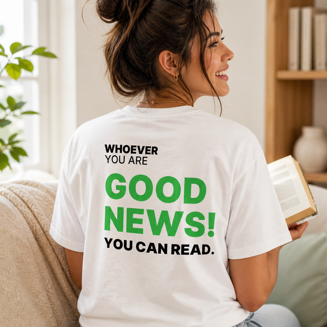 Person wearing a white Good News! You Can Read funny t-shirt while reading at home