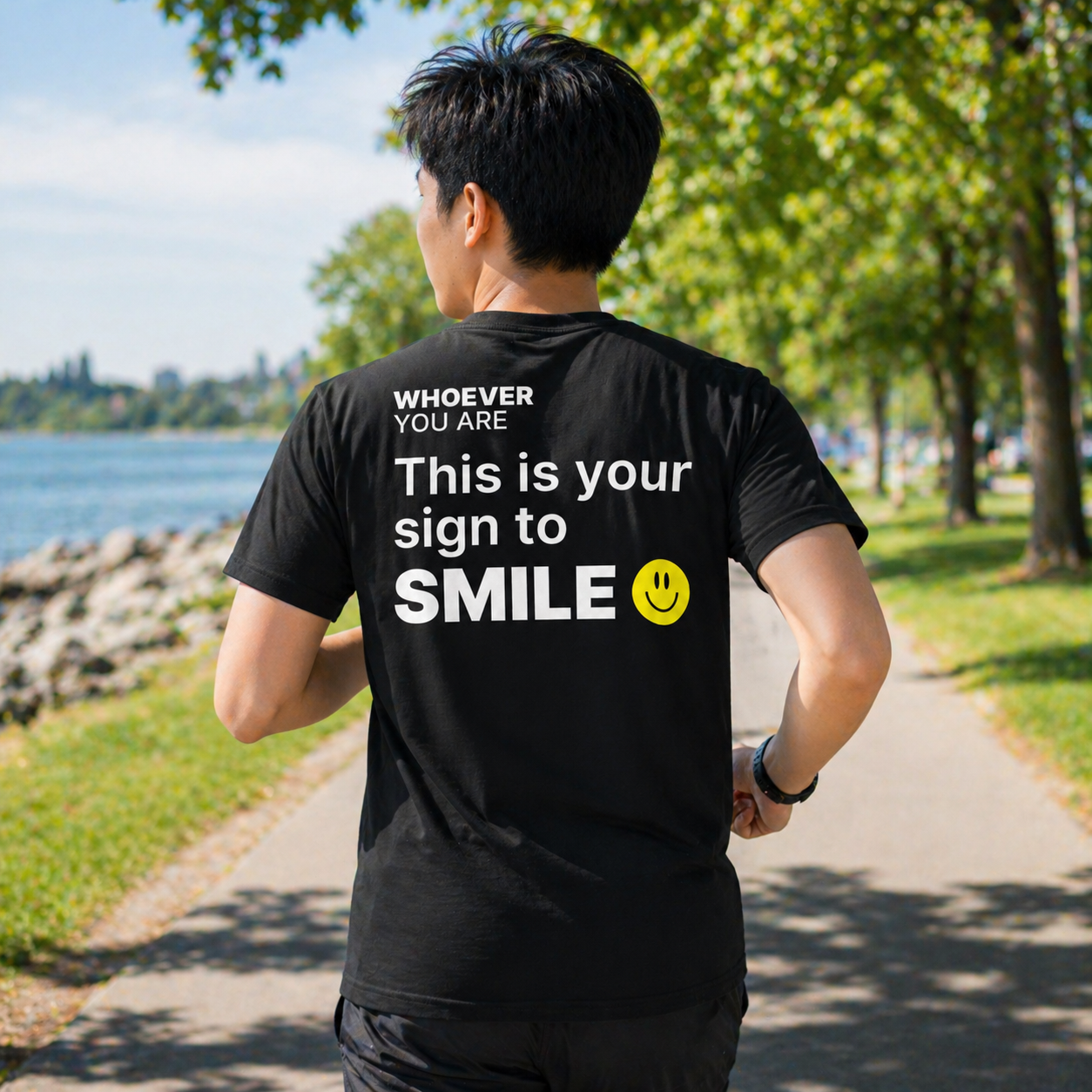 Person wearing a black This Is Your Sign to Smile t-shirt outdoors with back print visible