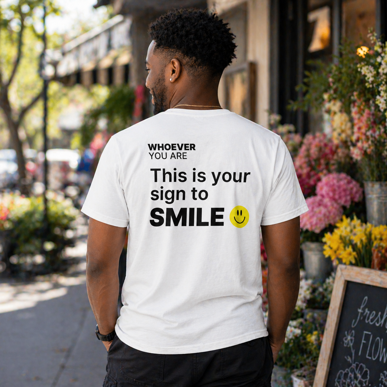 Person wearing a white This Is Your Sign to Smile t-shirt with cheerful back print in an outdoor setting