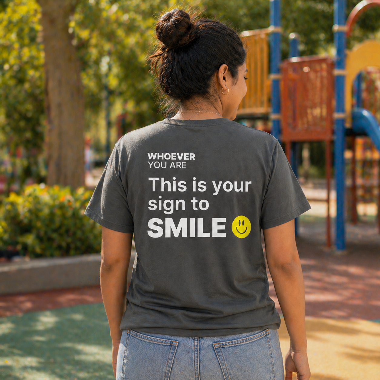 Person wearing a gray This Is Your Sign to Smile t-shirt in a park setting