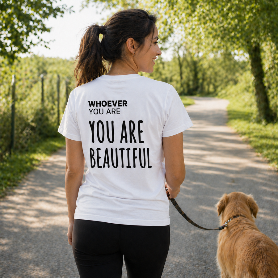 Person wearing a white You Are Beautiful kindness t-shirt while walking a dog outdoors
