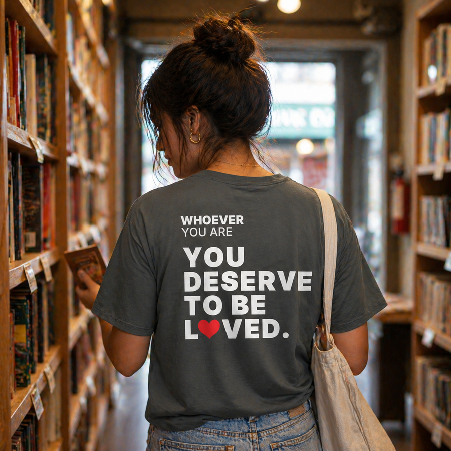 Person wearing a gray You Deserve to Be Loved kindness t-shirt with meaningful back print in a bookstore