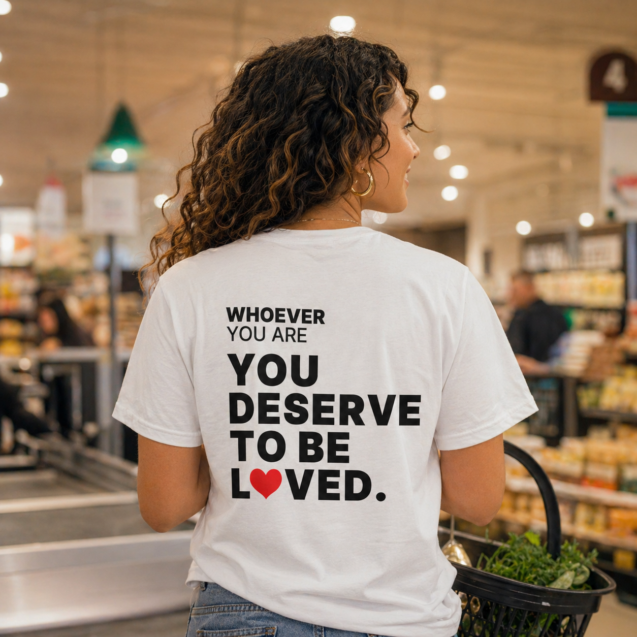 Person wearing a white You Deserve to Be Loved t-shirt outdoors with back print visible
